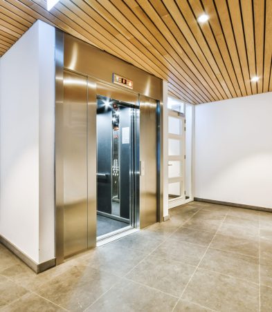 Shiny elevator with opened door located in illuminated hall of contemporary apartment building with tiled floor
