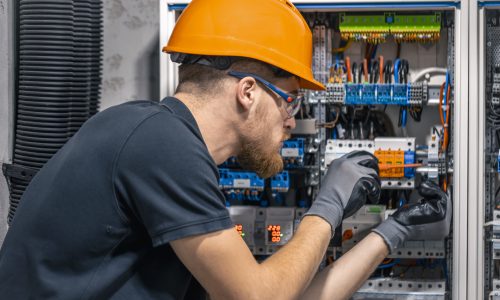 Male electrician working in a switchboard with fuses. Installation and connection of electrical equipment. Professional with tools in hand.